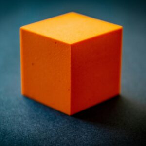 Close-up of an orange foam cube on a dark surface, highlighting its texture and color contrast.
